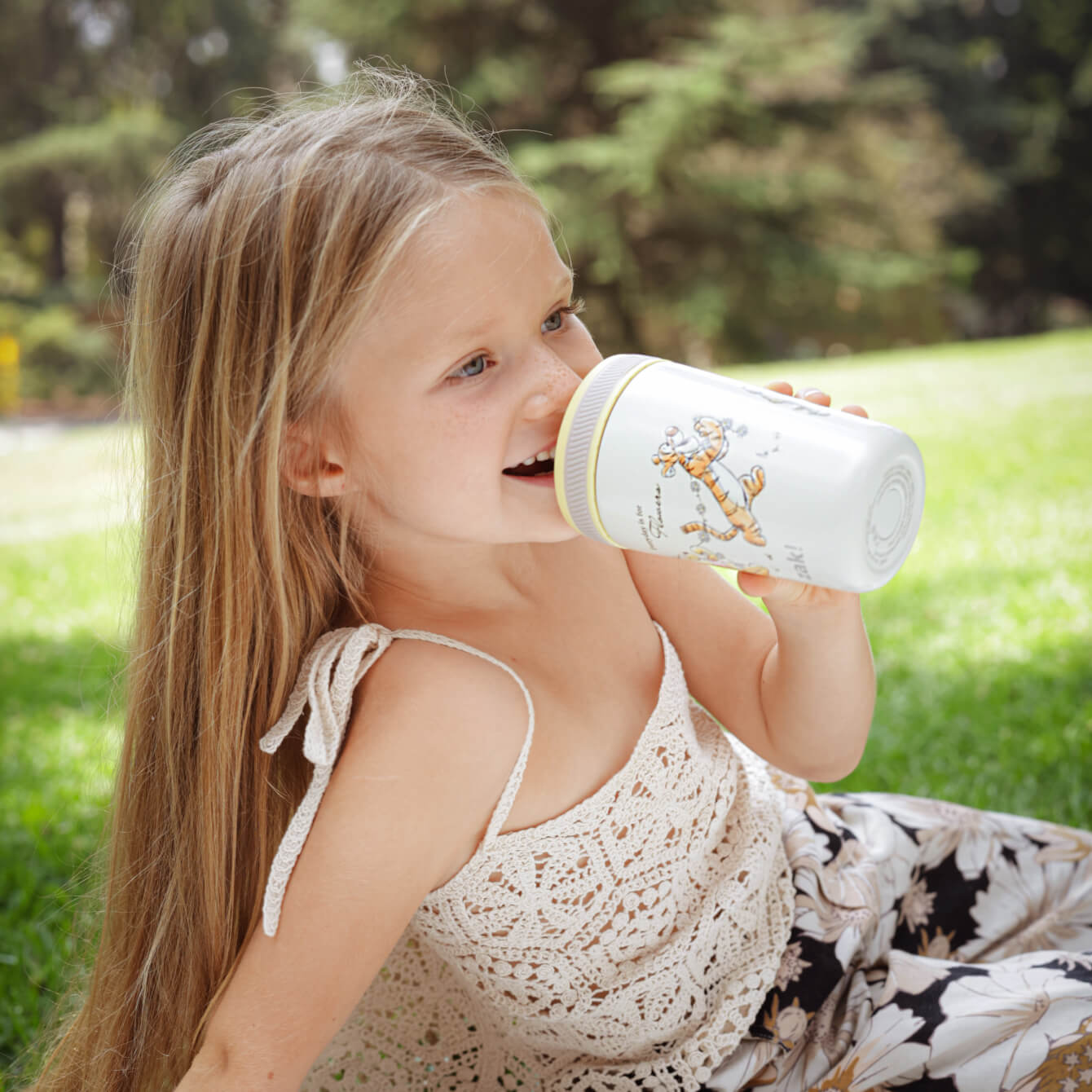 girl sitting outside sipping from a winnie the pooh cup