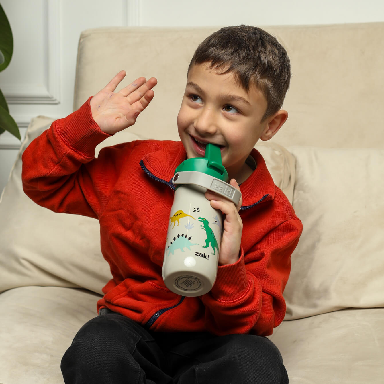 boy smiling while sipping from a dinosaur themed water bottle