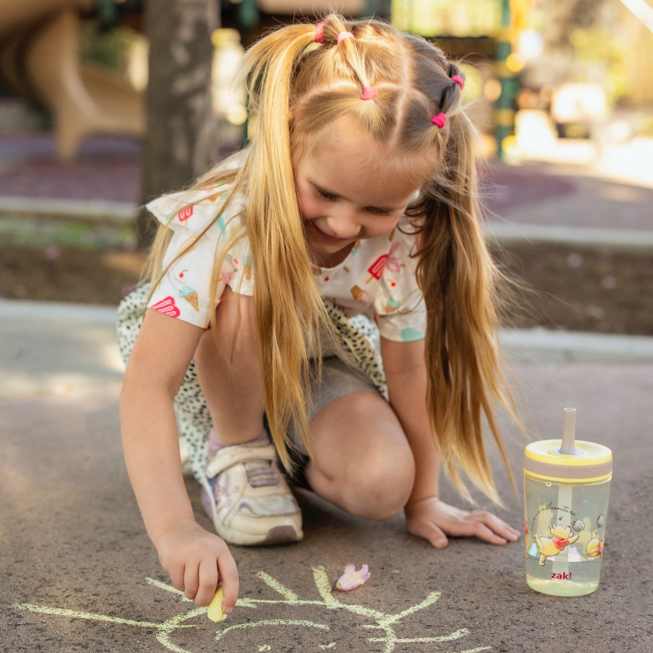 girl creating chalk art outside with cup nearby