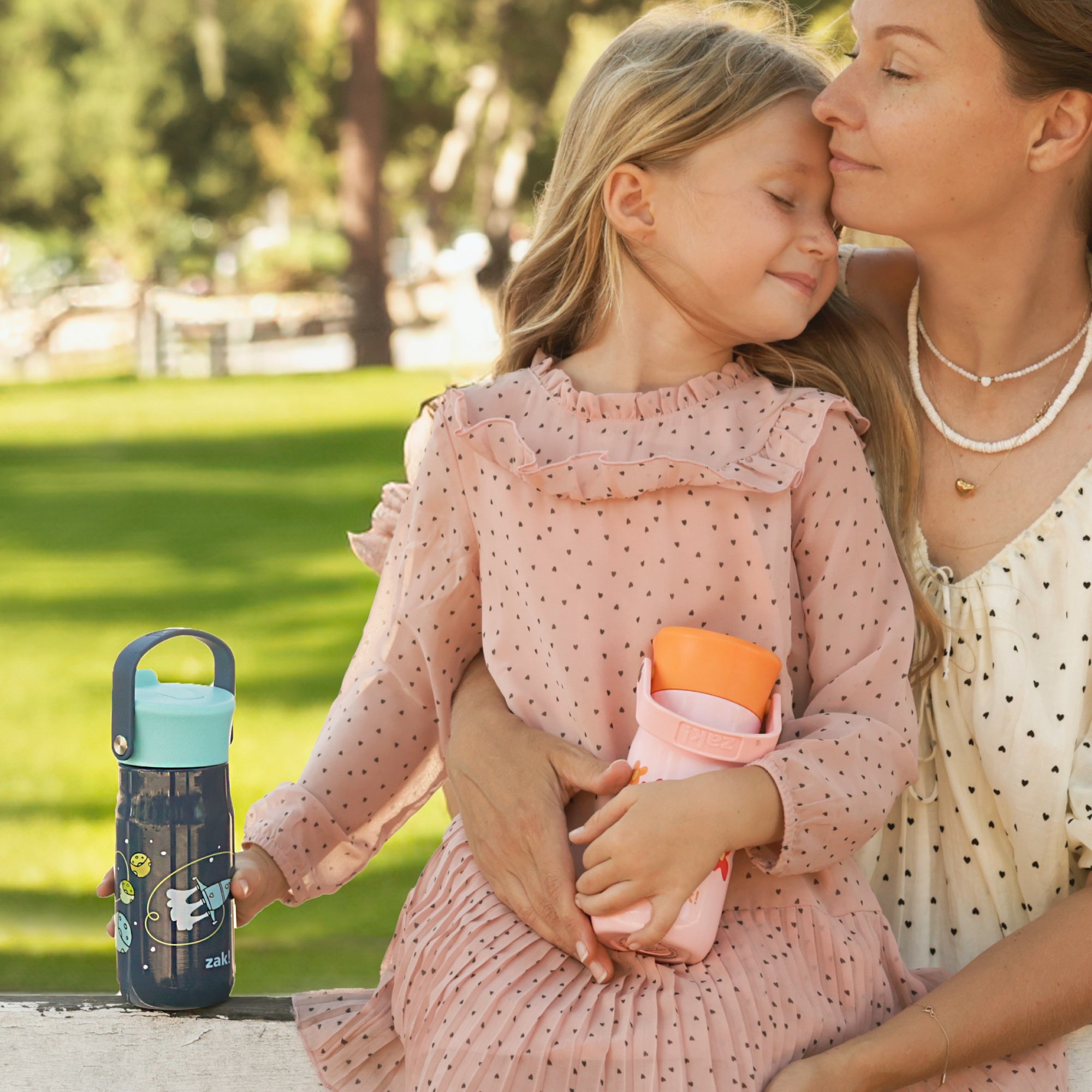 girl holding two colorful water bottles while sitting closely with her mother