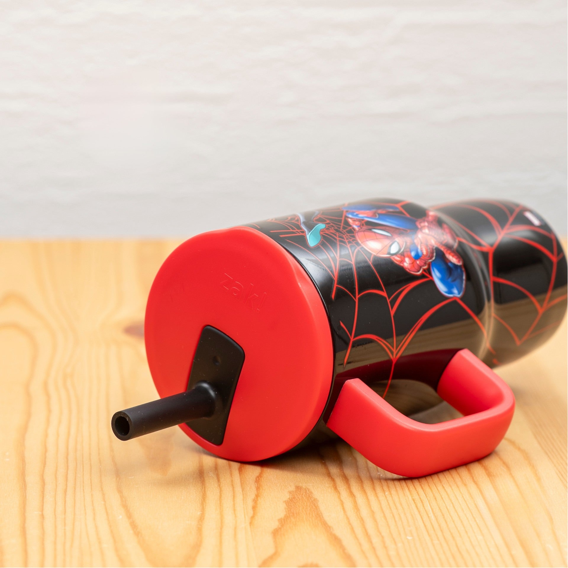 Kids Spider-Man straw tumbler laying on side on light wood tabletop