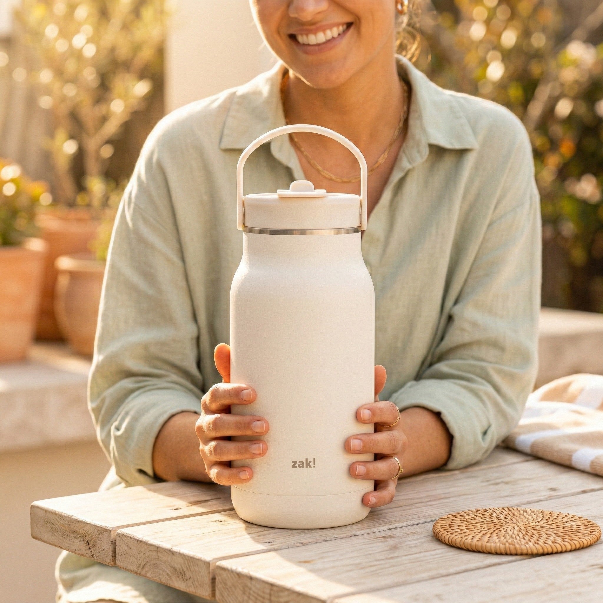 Person holding a white insulated bottle with a handle outdoors