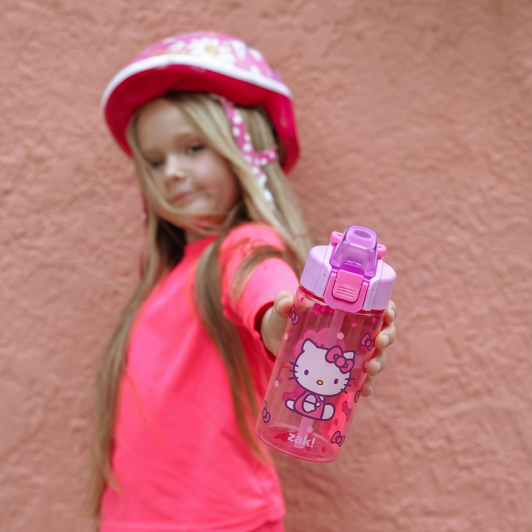 girl holding pink Hello Kitty water bottle in front of pink wall