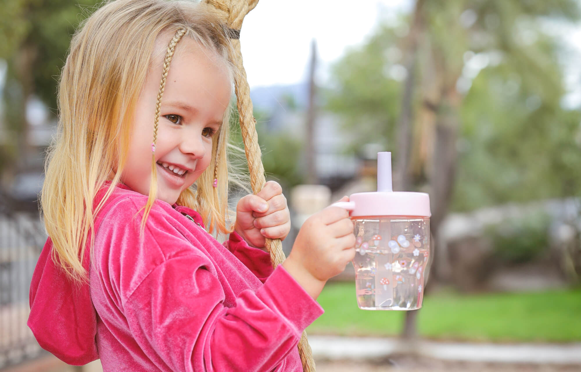 Child holding a pink zak tumbler with a straw in an outdoor setting