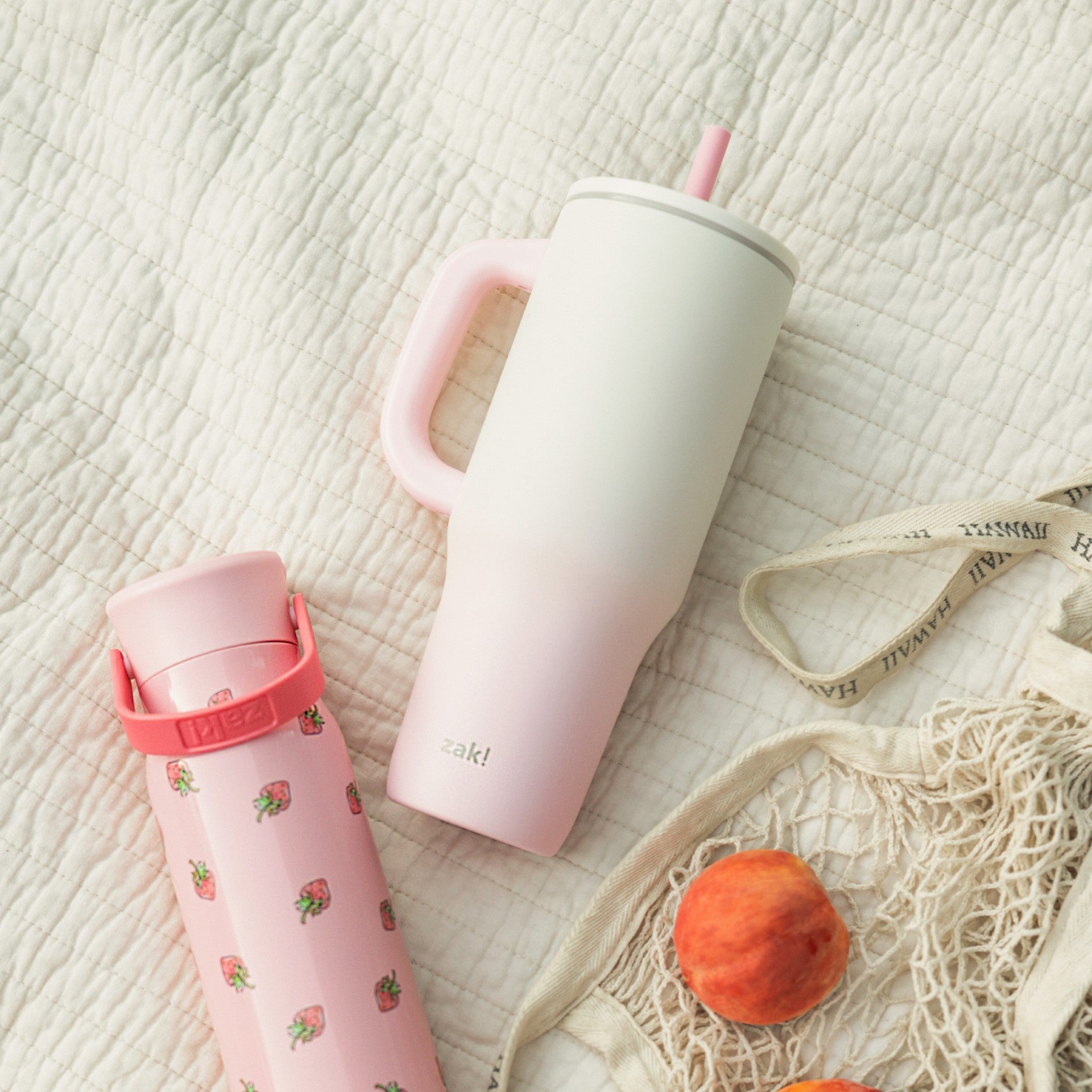 Pink and white large open top tumbler and pink water bottle laying on a cream blanket