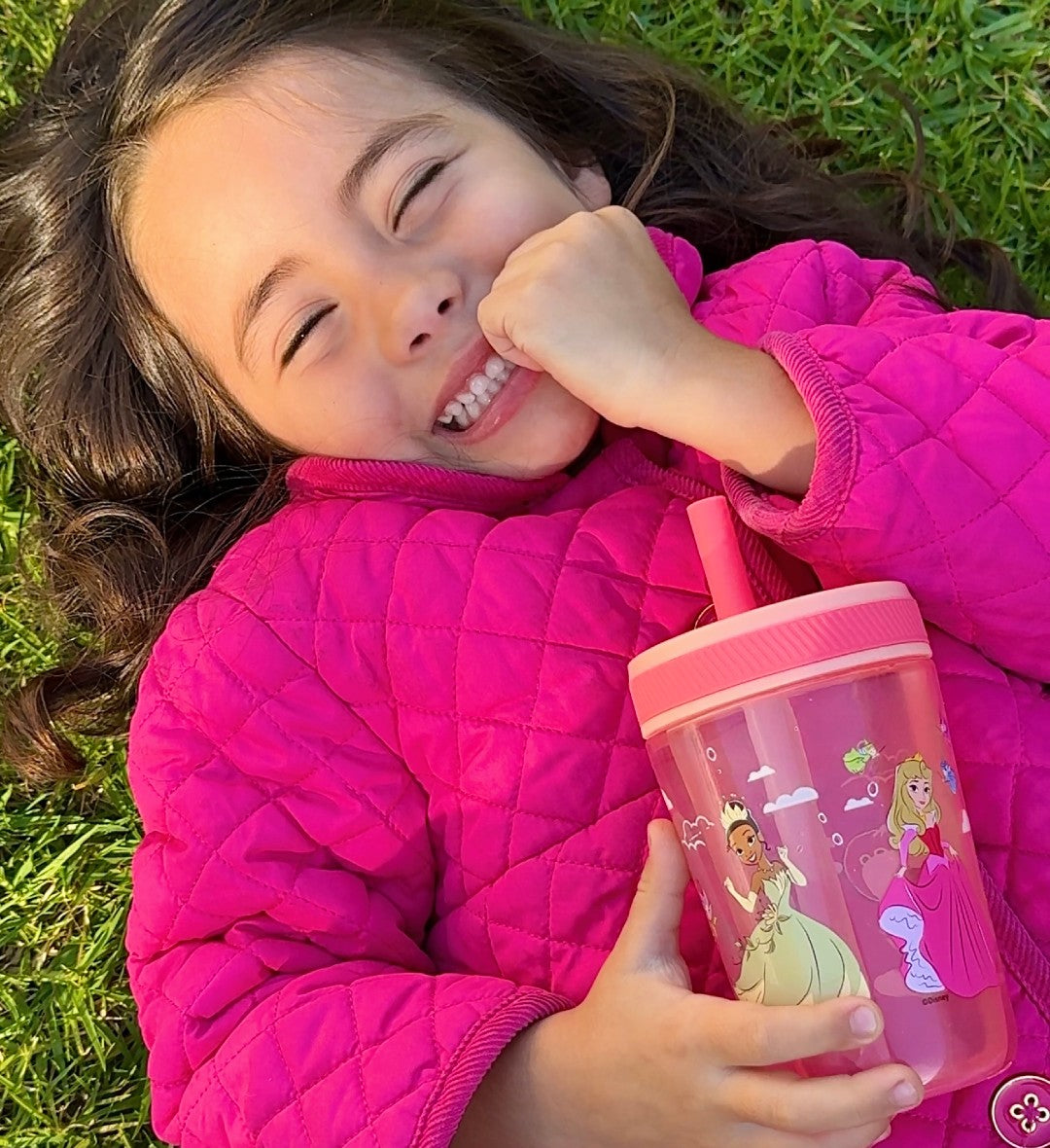 Child in pink jacket holding a pink Zak Designs tumbler with princess designs on grass