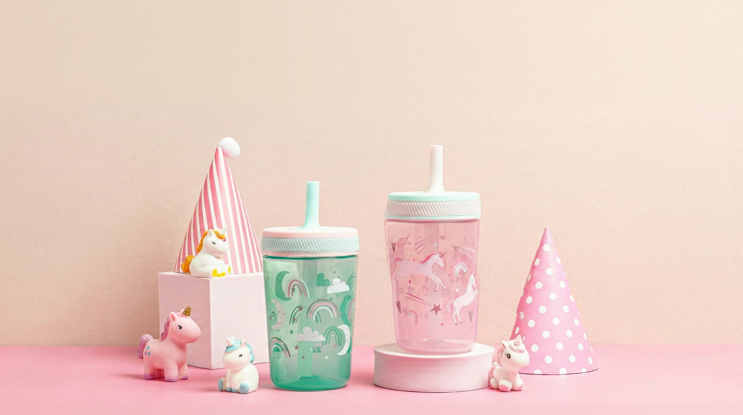 Two colorful zak tumblers with straws on a pink surface with small decorative items.