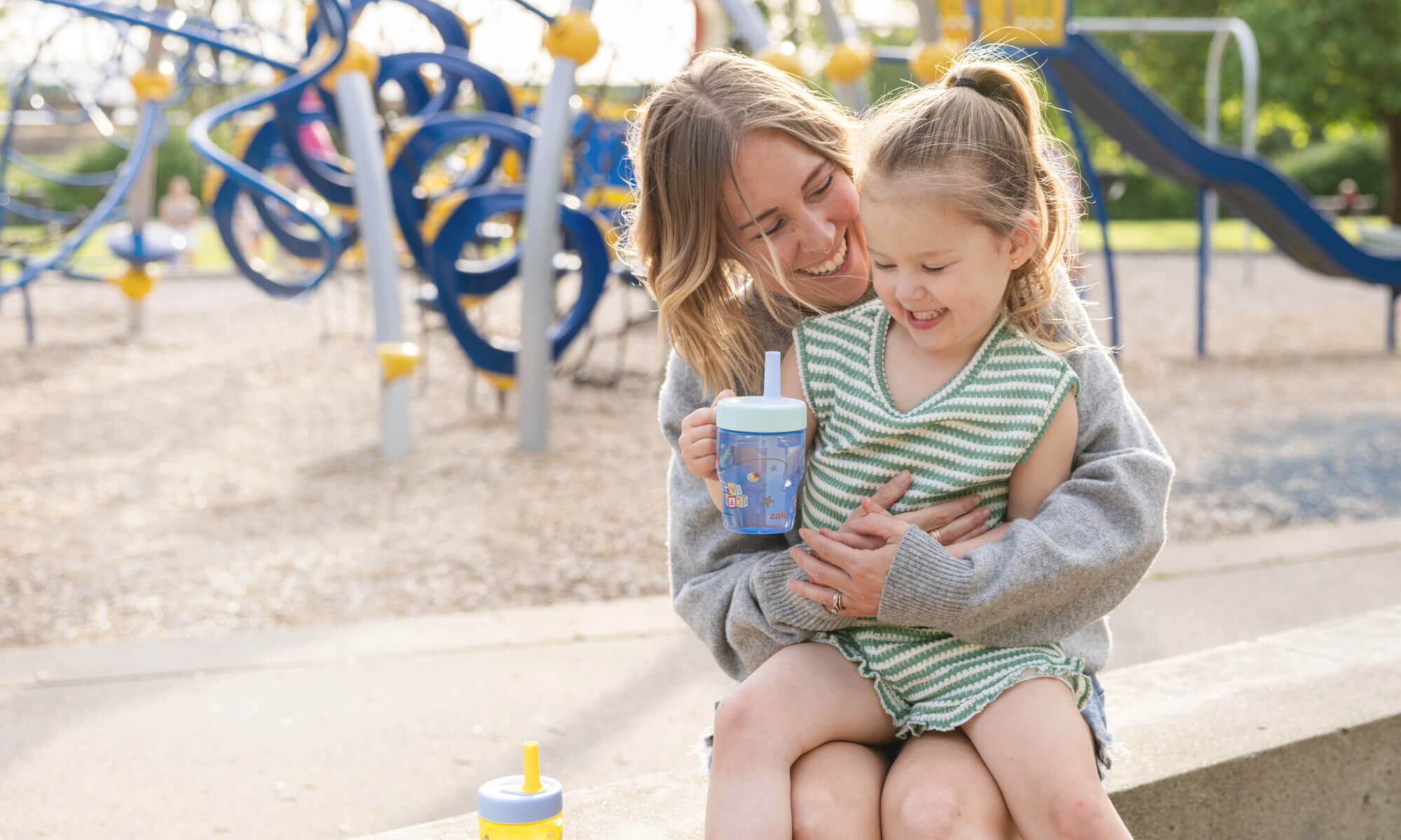 Child sitting on mother's lap holding a blue sippy cup