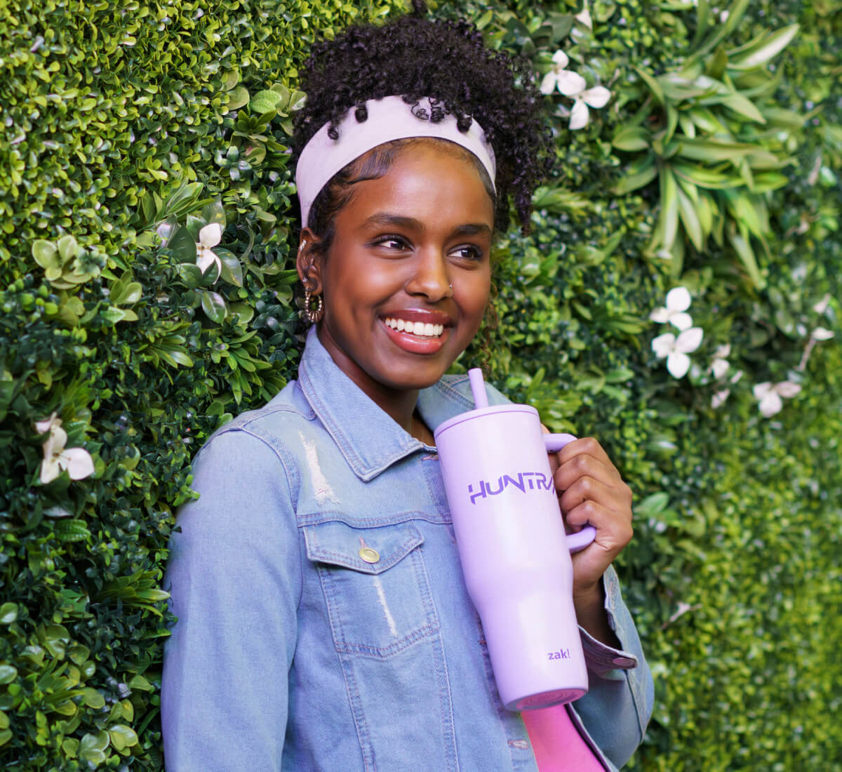 smiling woman in front green wall holding a purple kpop demon hunters zak tumbler