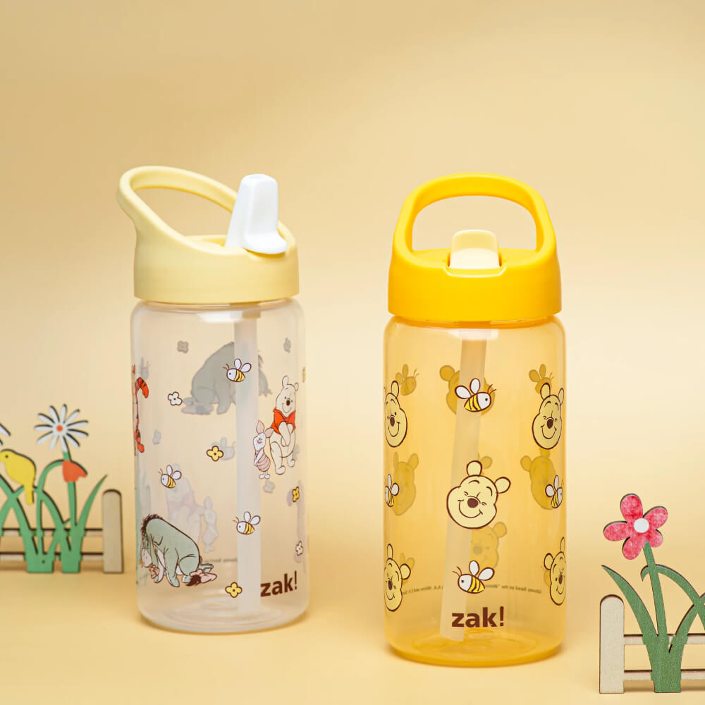 Two cartoon water bottles on a warm beige background. The left bottle is clear with a pale yellow lid and printed animal illustrations; the right bottle is translucent yellow with a bright yellow lid and bear-face prints.