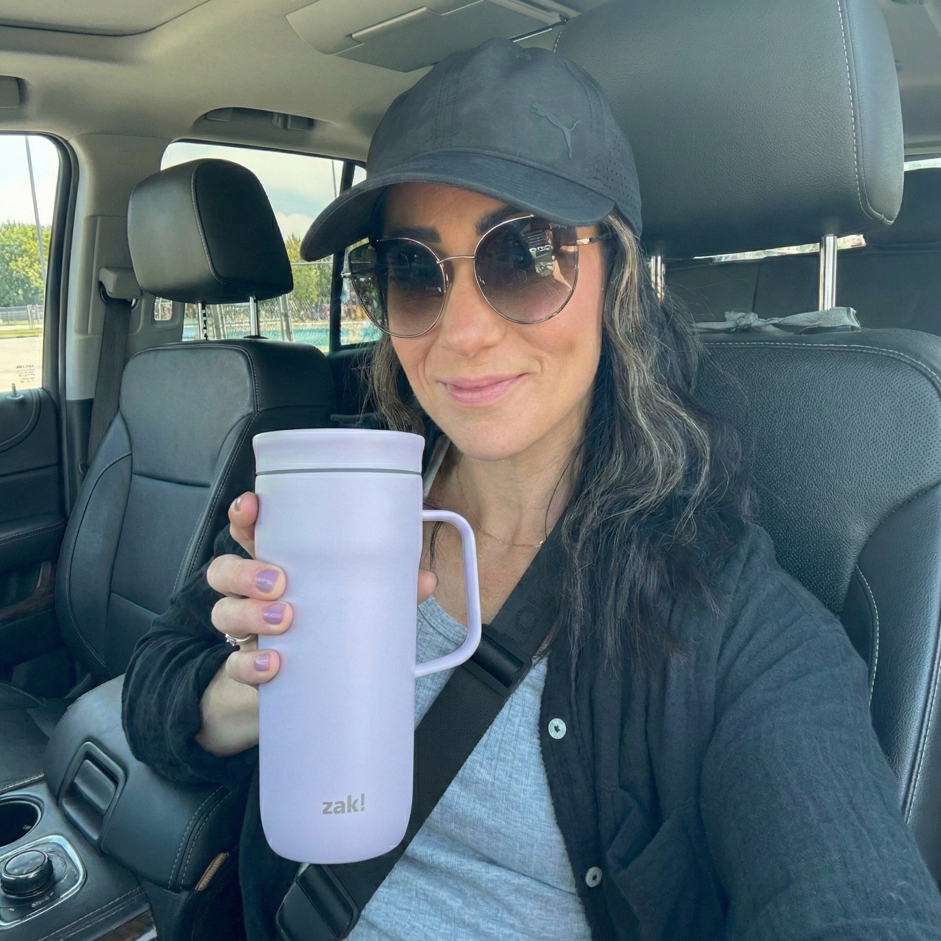 Woman in a car holding a white mug with 'zaki' branding