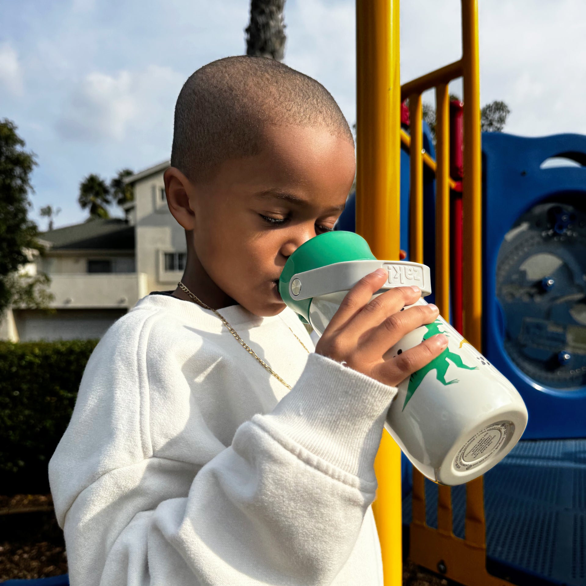 Child drinking from a white and green sippy cup on a playground