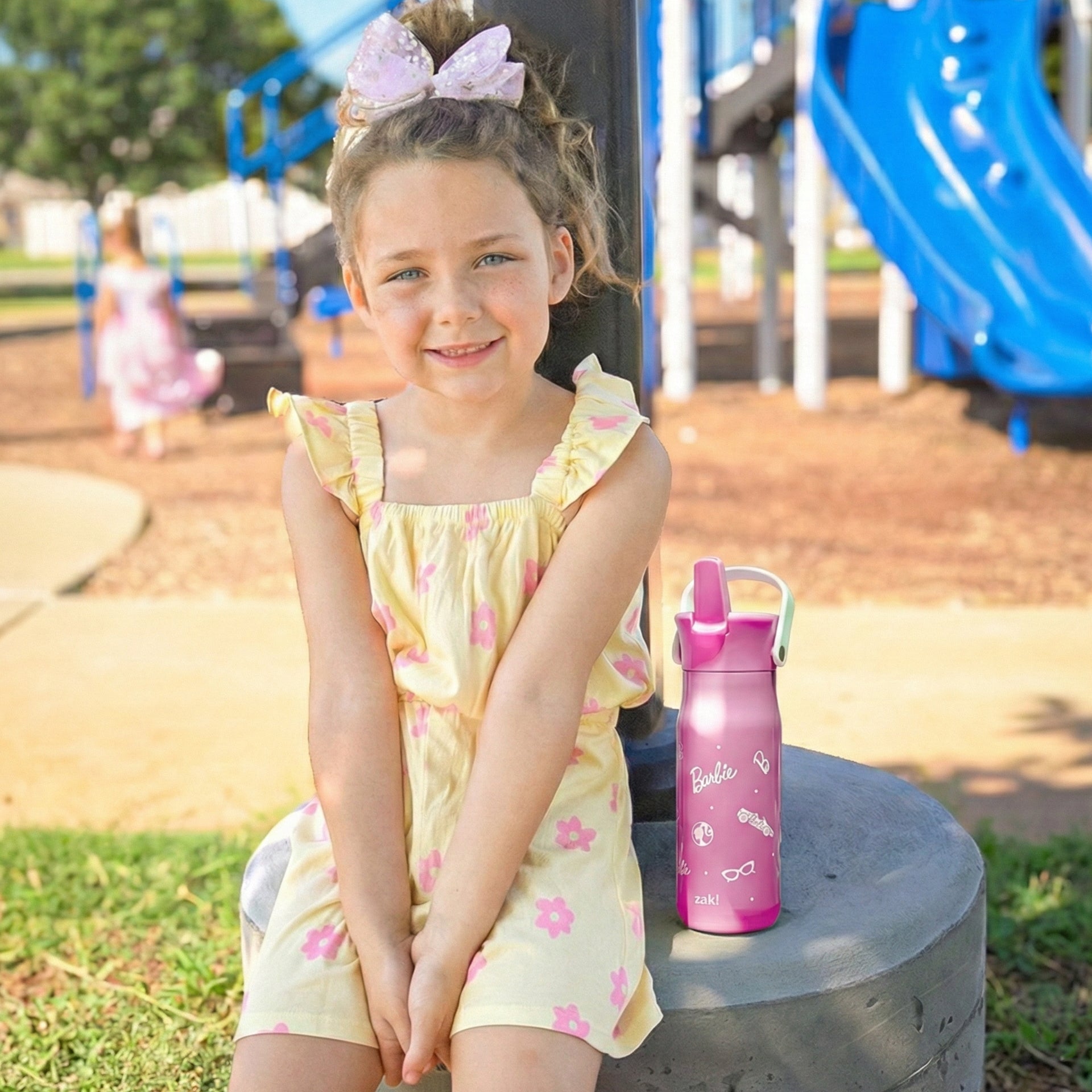 Girl at a park sitting next to Barbie water bottle with flip up spout
