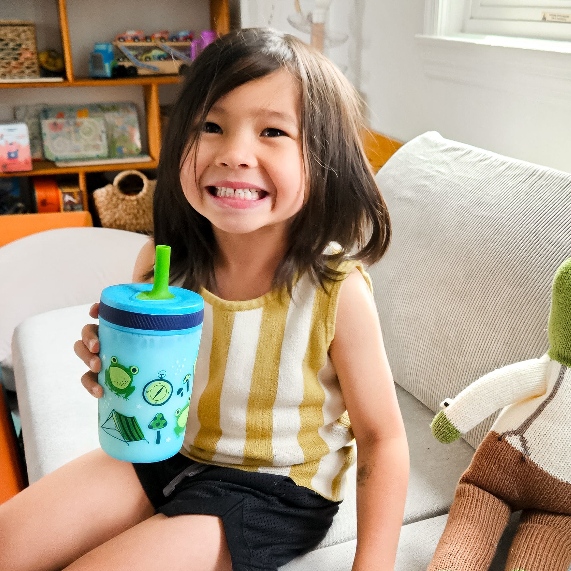Child holding a blue tumbler with green frog design on a couch
