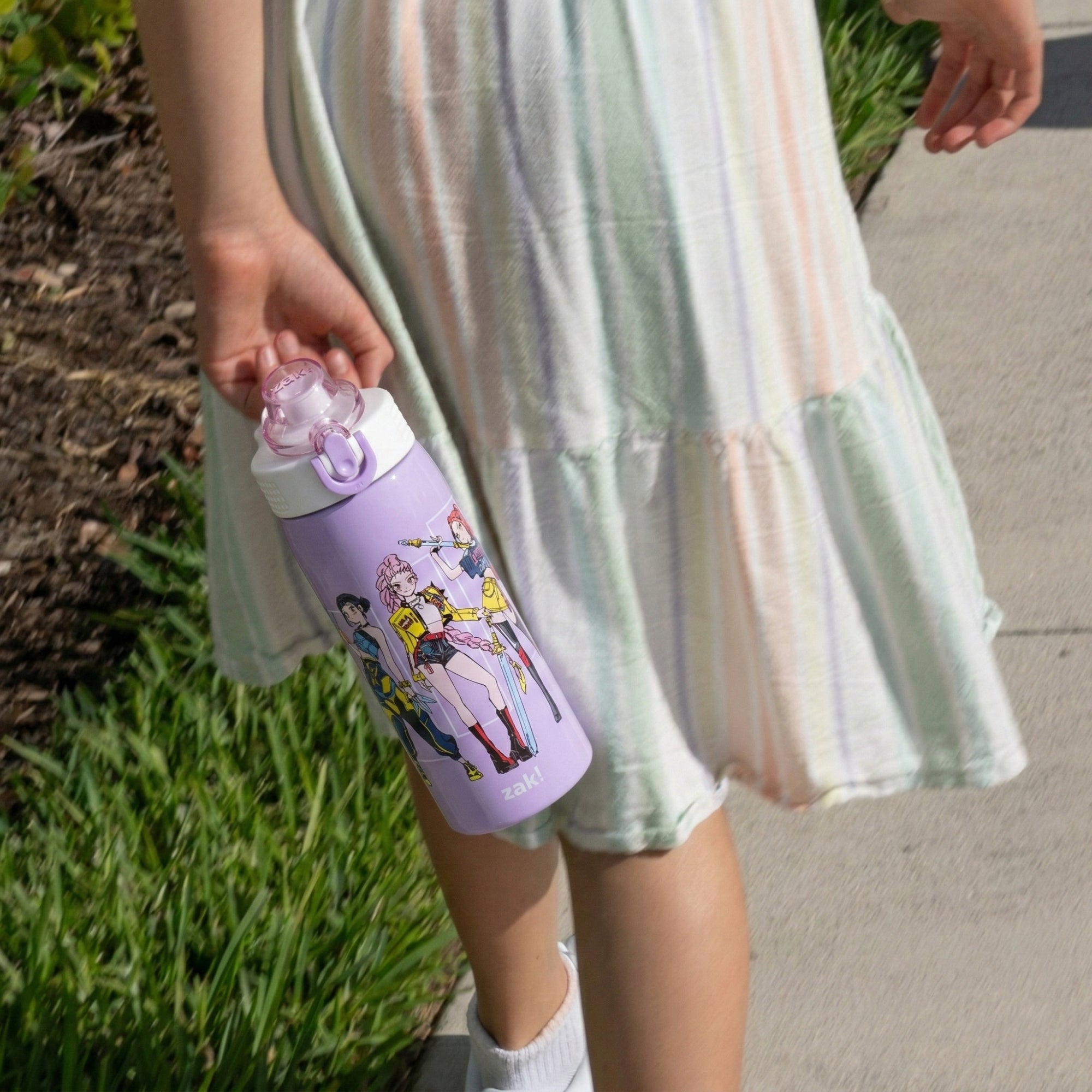 Girlholding a purple water bottle with cartoon characters on a grassy area