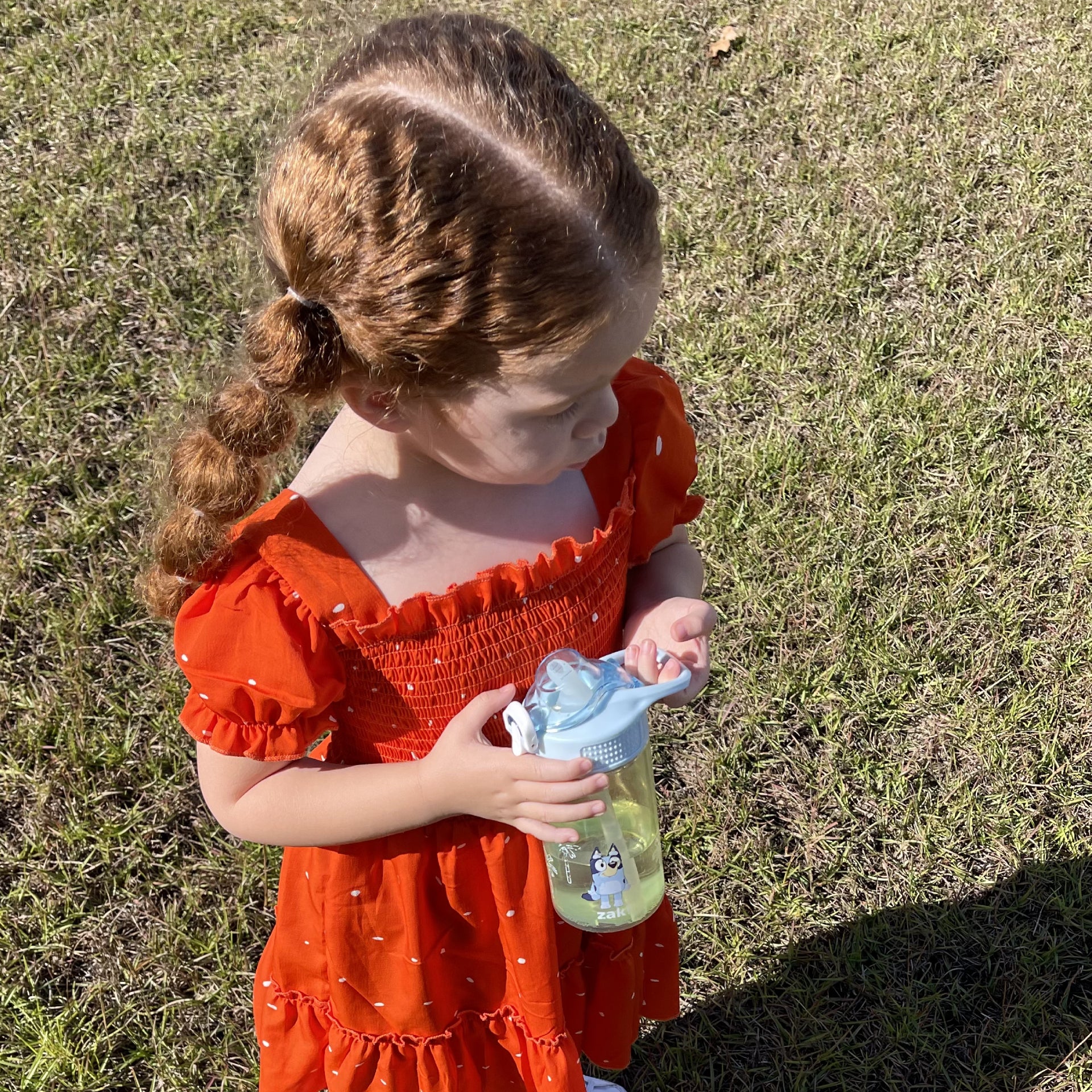 Girl in orange dress holding a green and blue kids water bottle