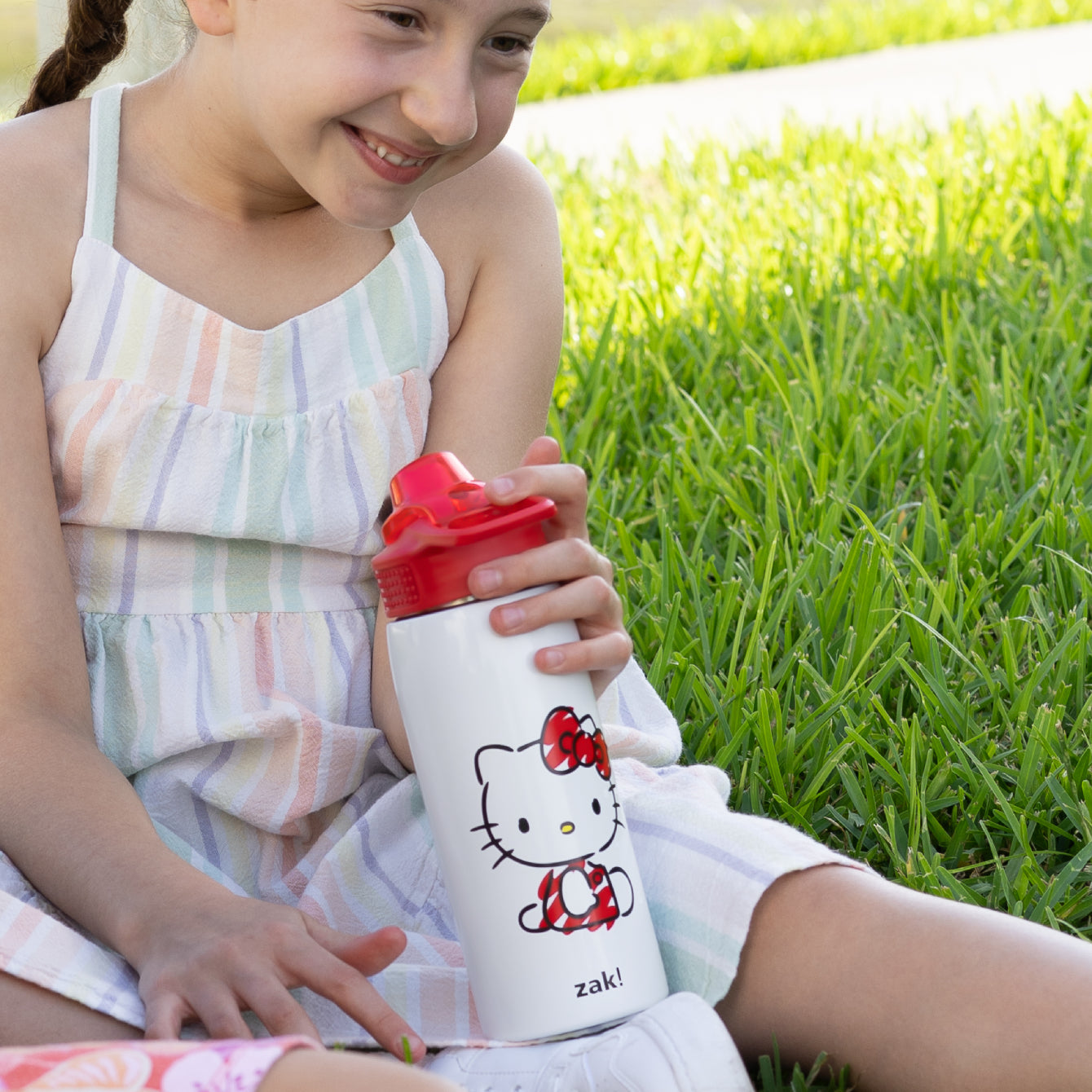 girl sitting in grass holding a white and red water bottle
