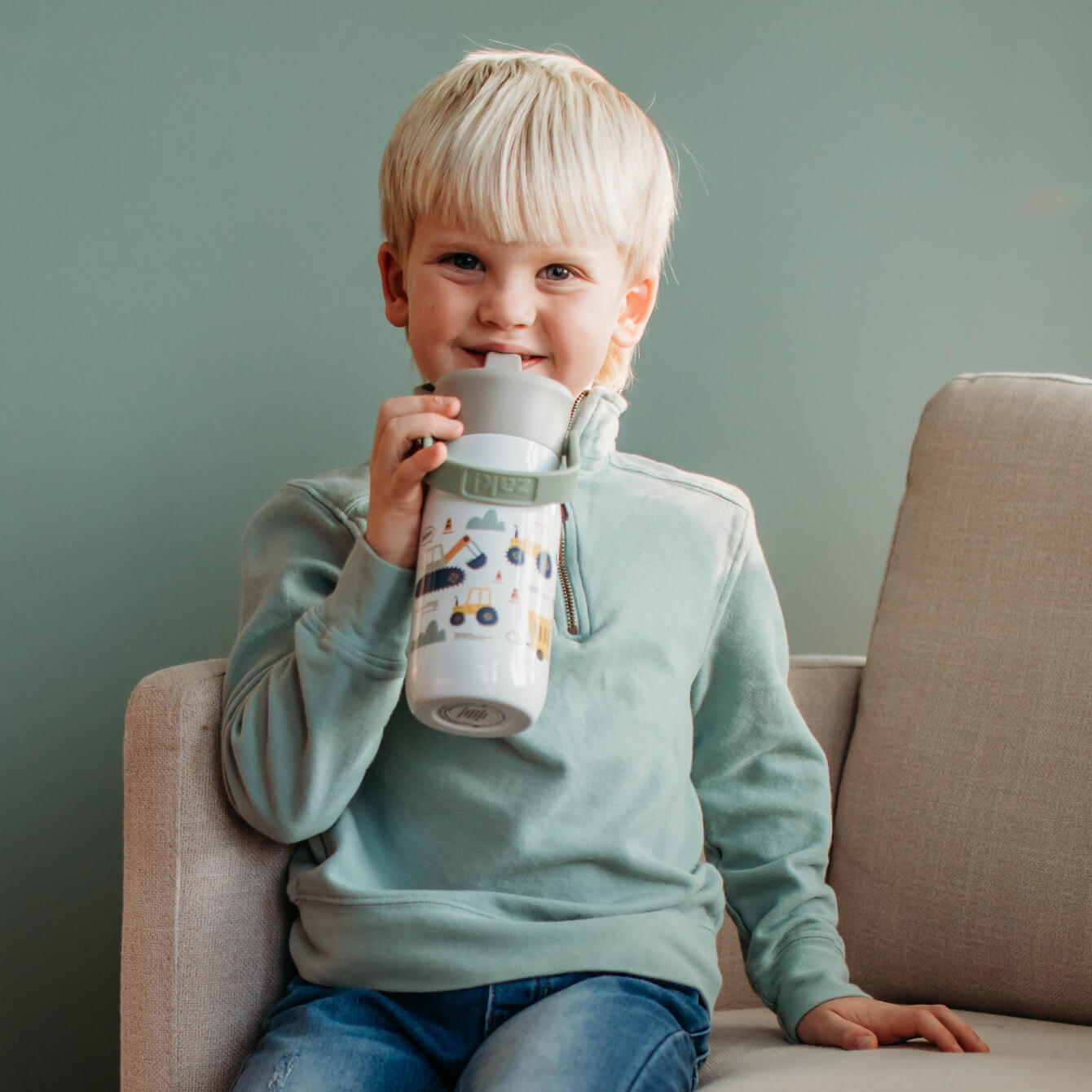 boy sitting on couch drinking from a white and green tumbler