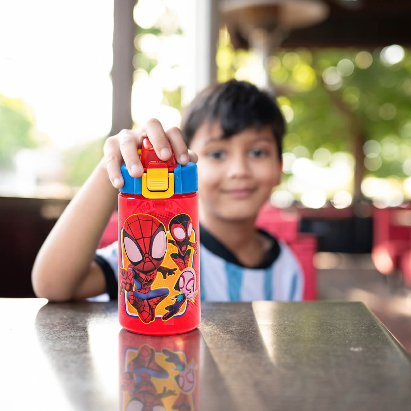 boy at a table holding a spiderman water bottle