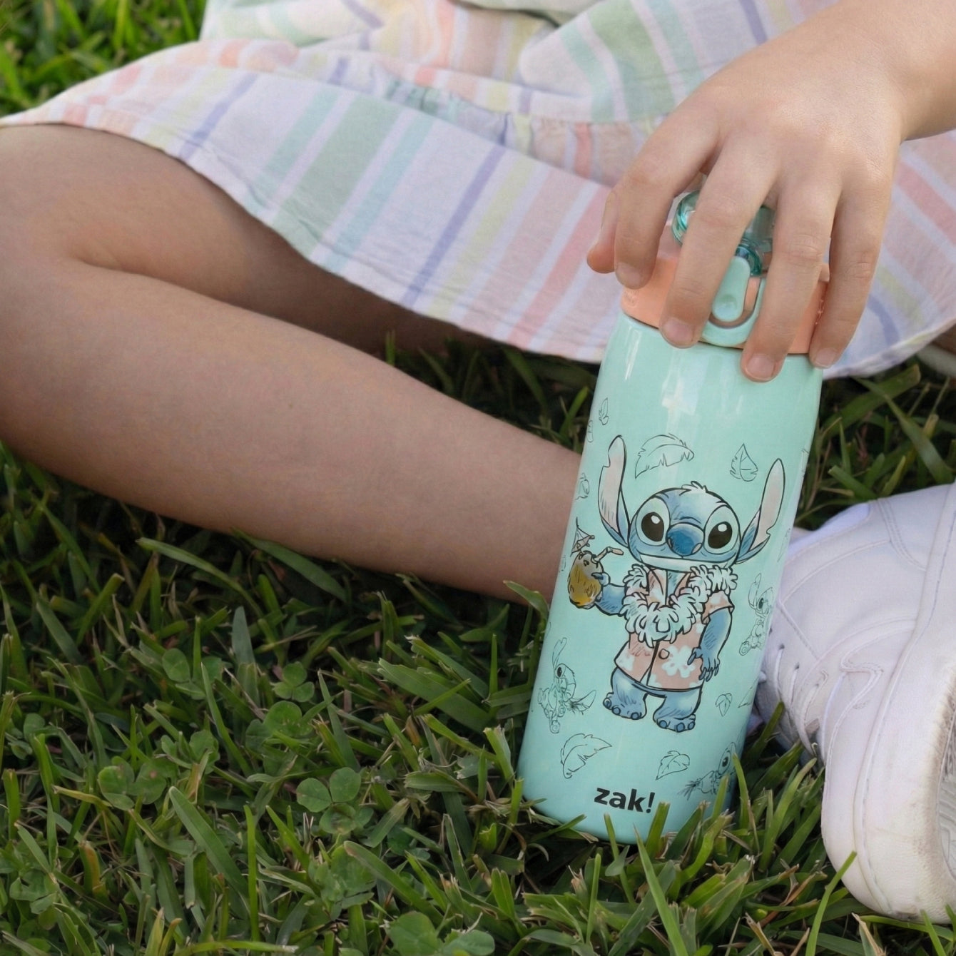 kid in grass holding a green lilo and stich water bottle