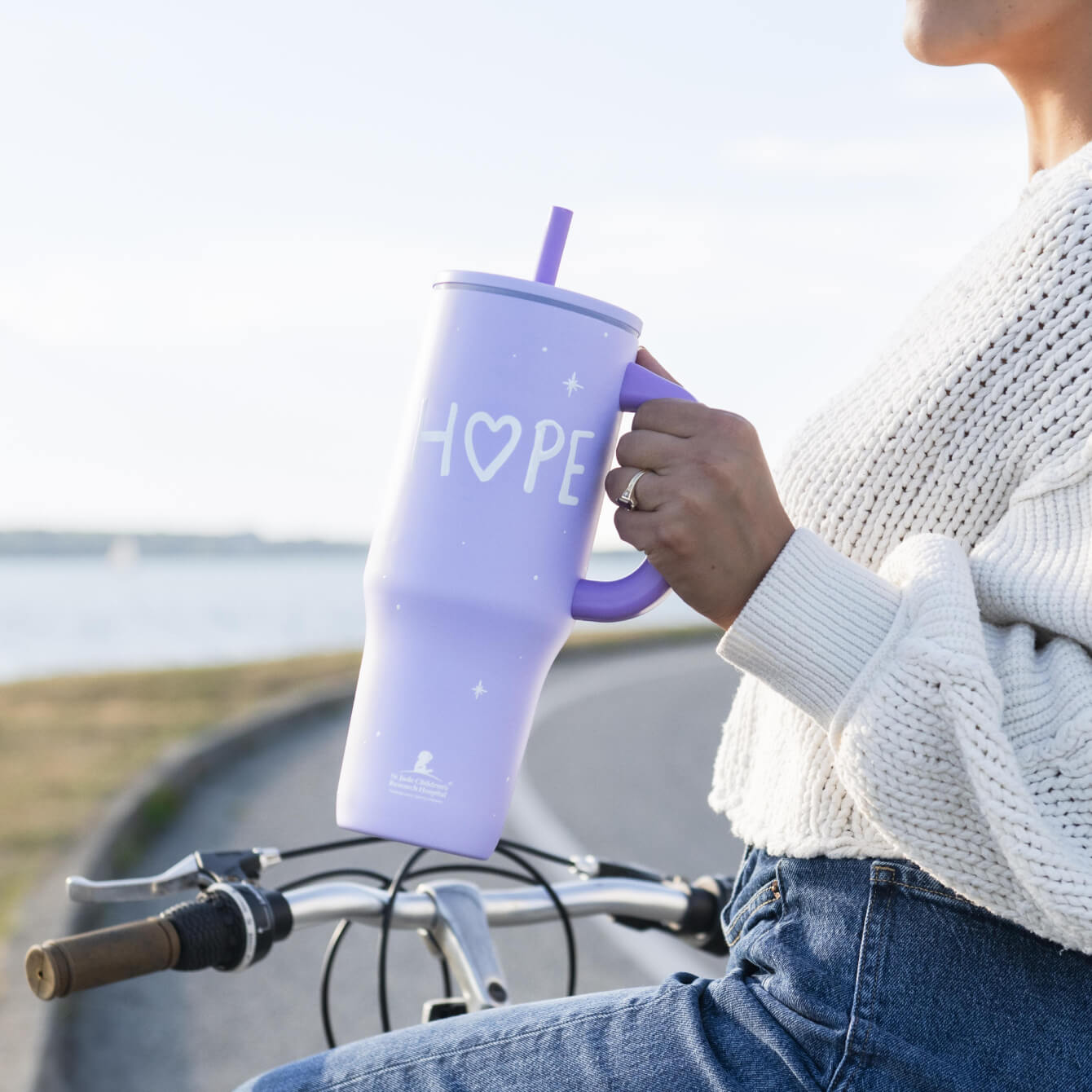woman on bicycle holding a purple tumbler with Hope design