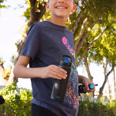 Boy standing next to bicycle holding a black and blue water bottle