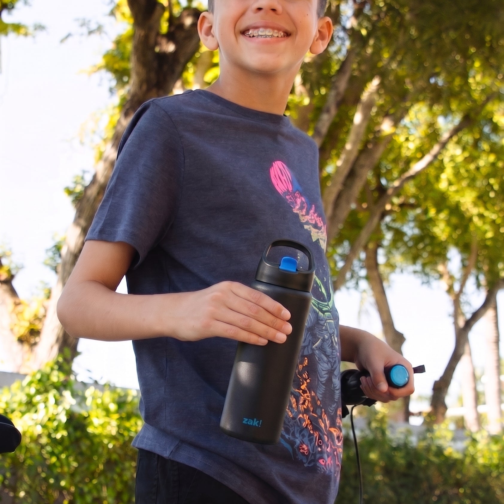 Boy standing next to bicycle holding a black and blue water bottle