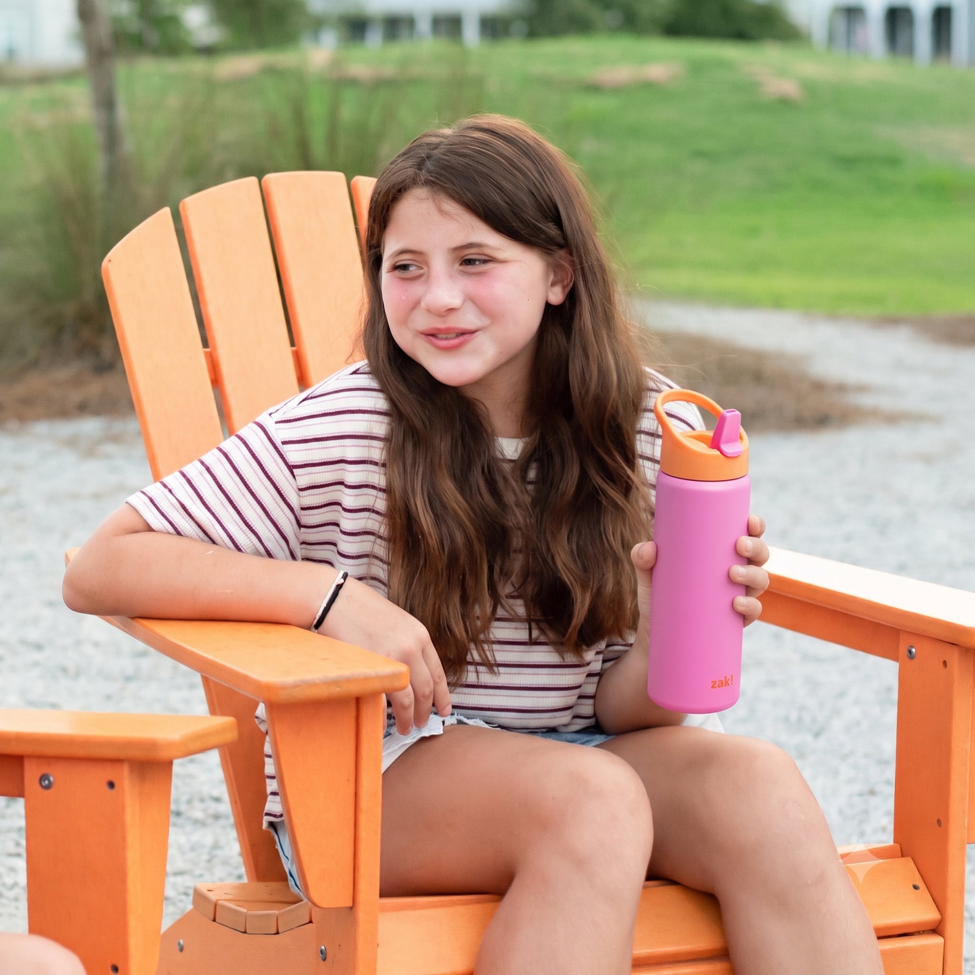 Smiling girl sitting in chair holding bright pink and orange water bottle