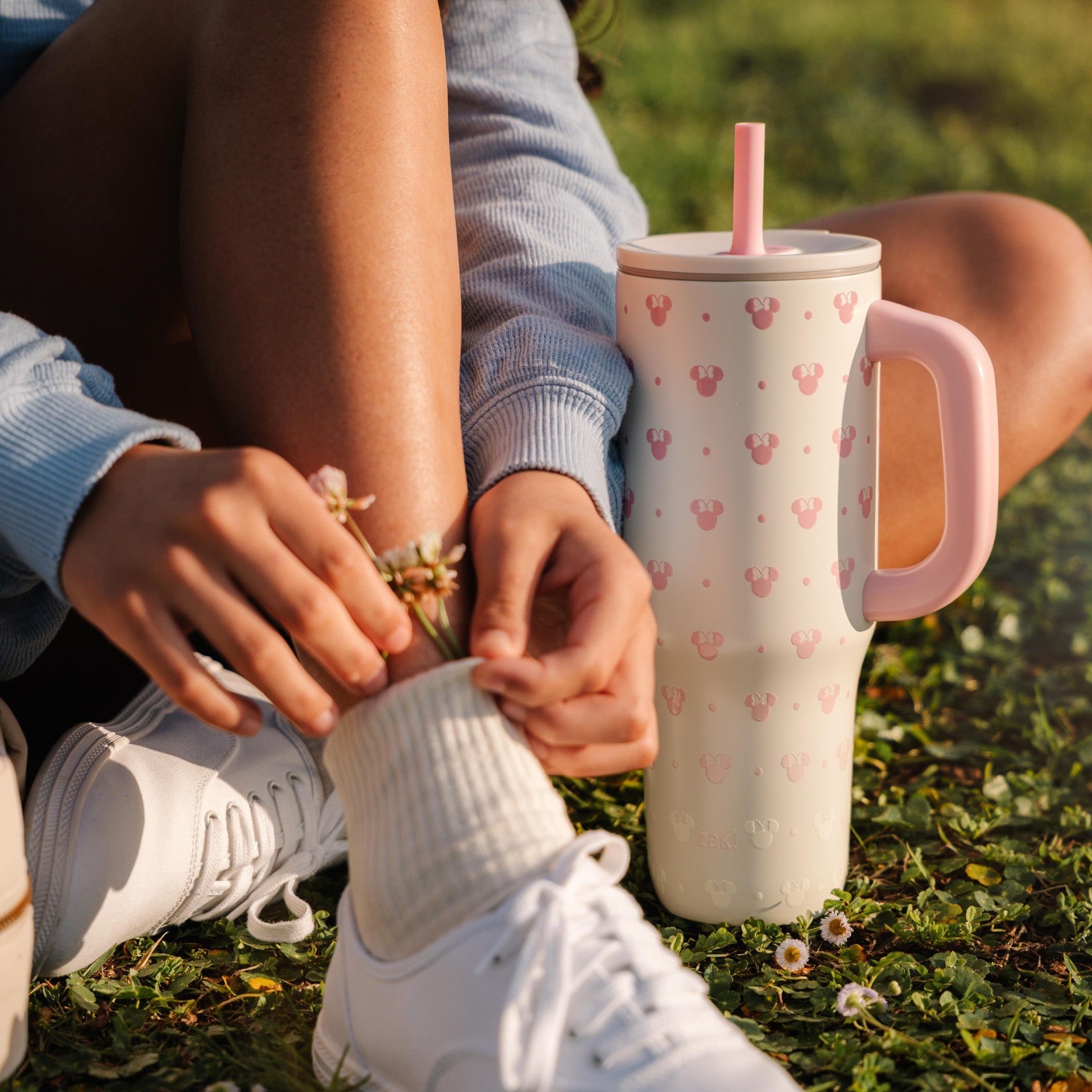 Woman sitting on grass with a pink tumbler featuring a cartoon character.