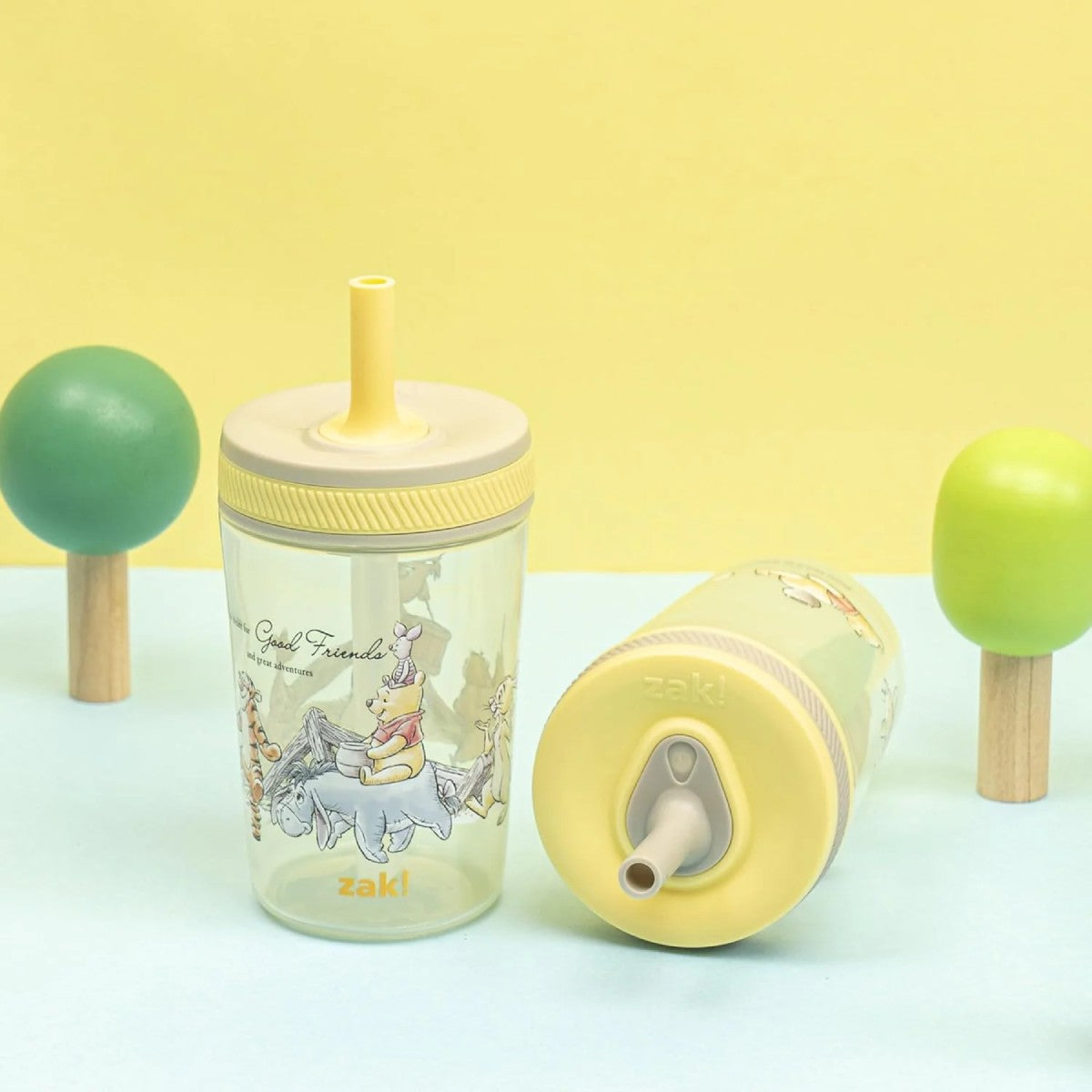 Two children's cups with straw lids on a light blue surface against a yellow background