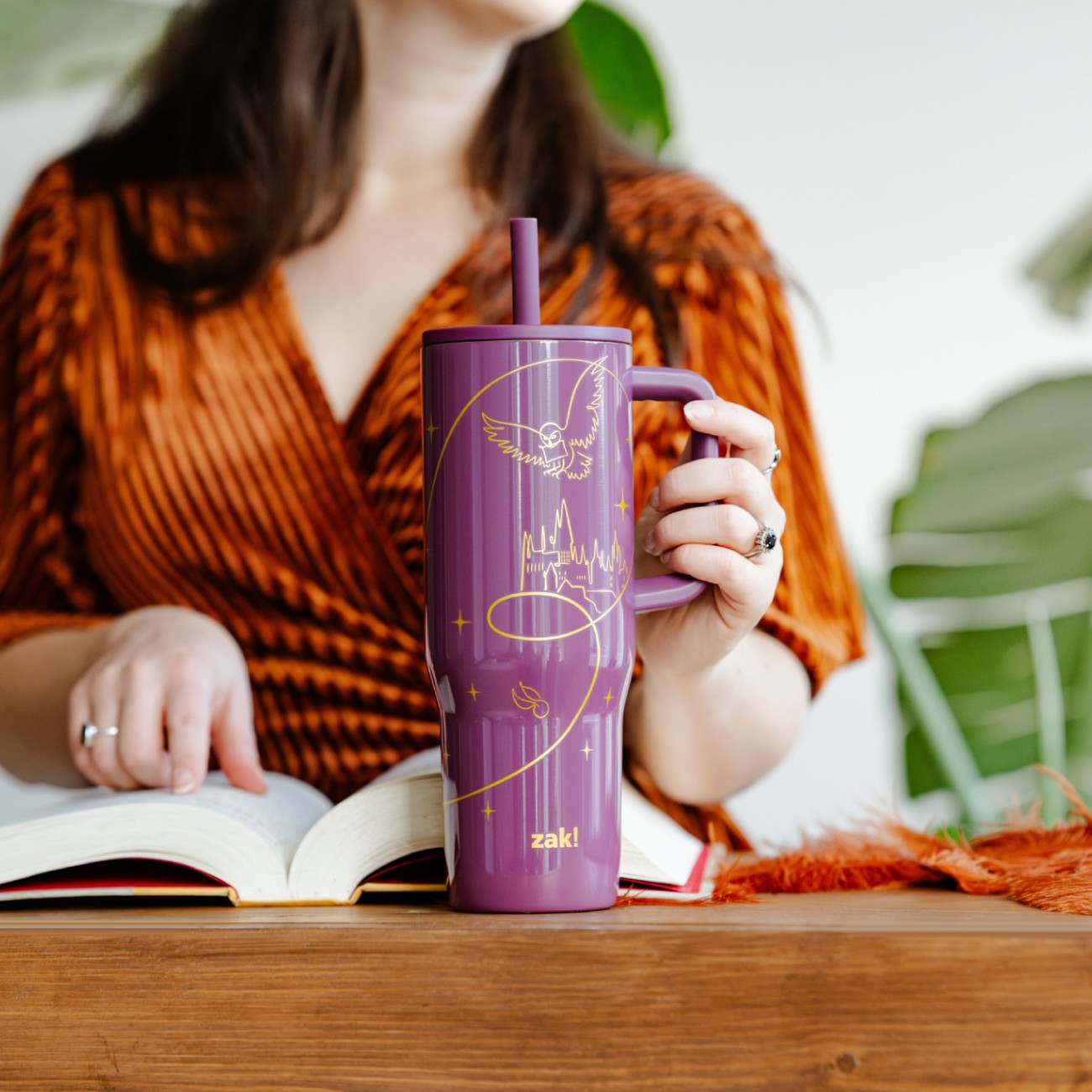 Person holding a Harry Potter tumbler with a straw, sitting at a table with an open book.