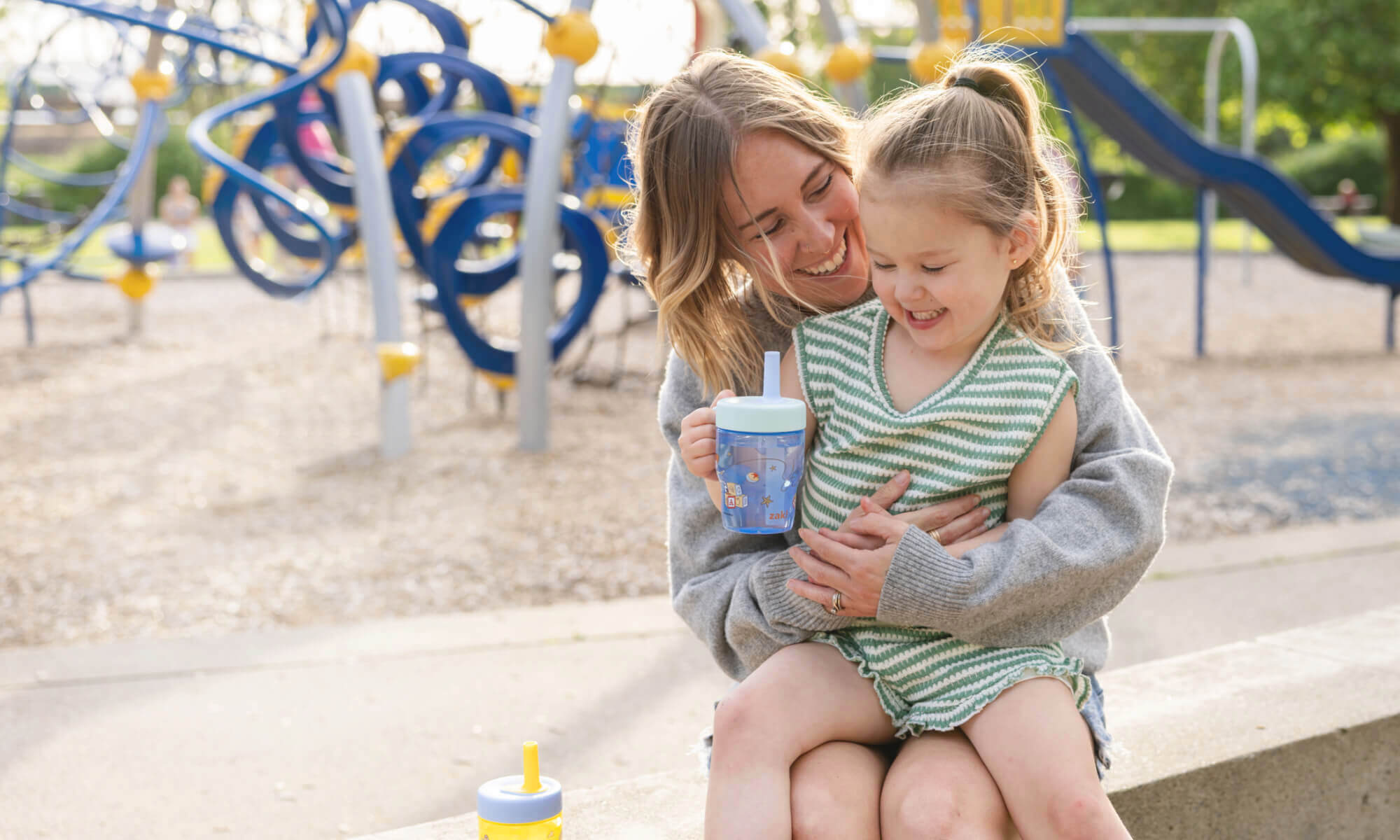 Child sitting on mother's lap holding a blue sippy cup
