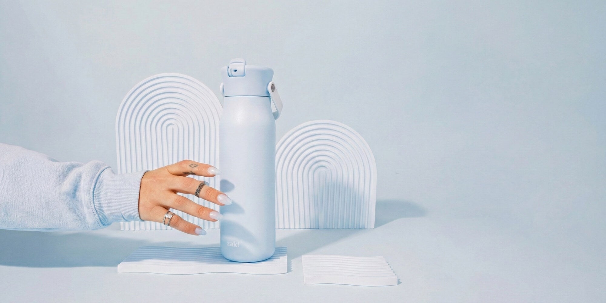 Light blue zak water bottle held by a hand on a light blue background