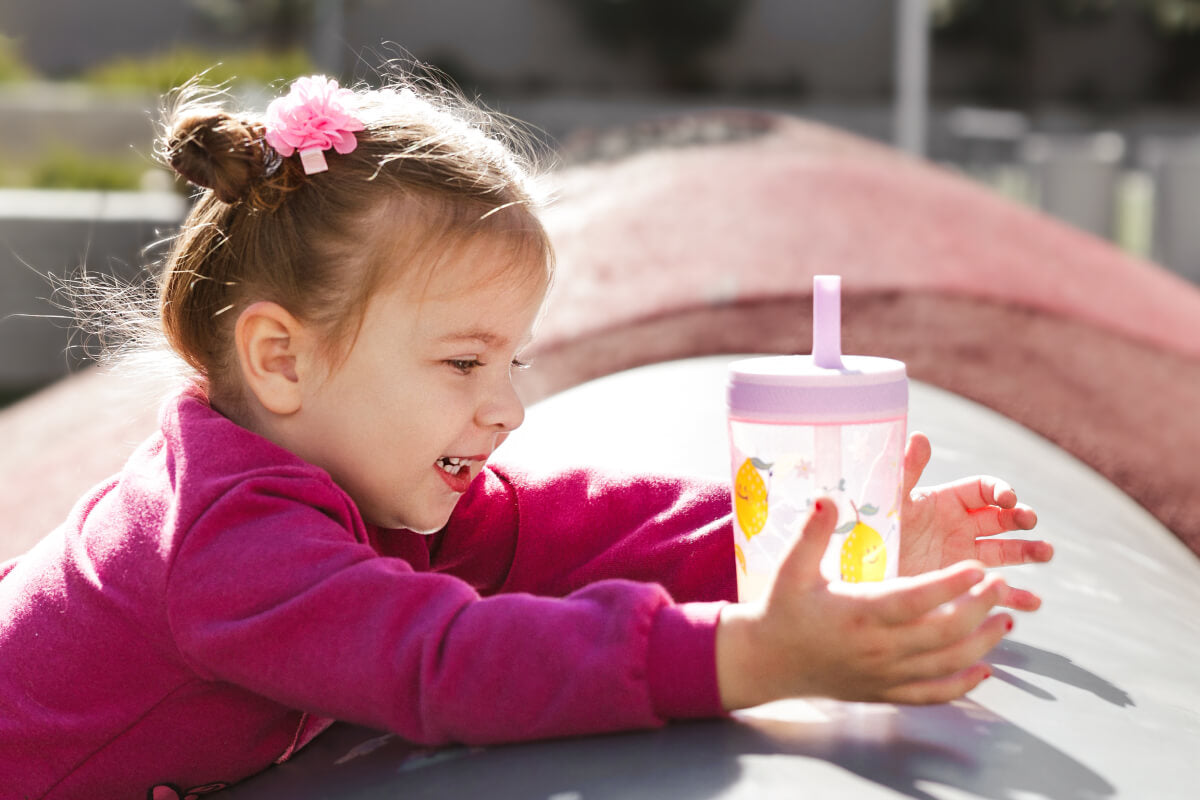 Child holding a colorful zak tumbler with a straw outdoors