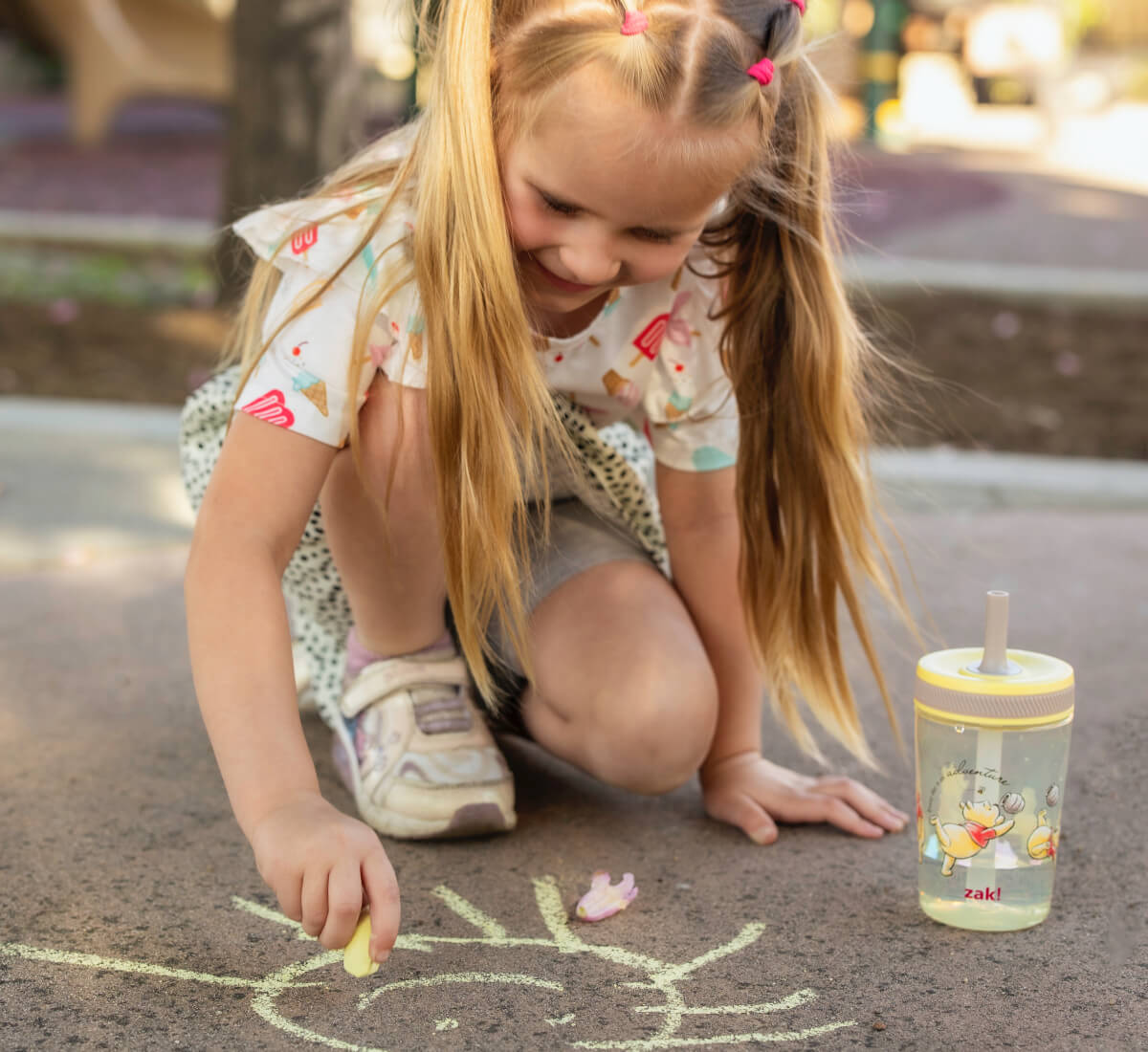 Child drawing on pavement with a zak Winnie the Pooh tumbler nearby
