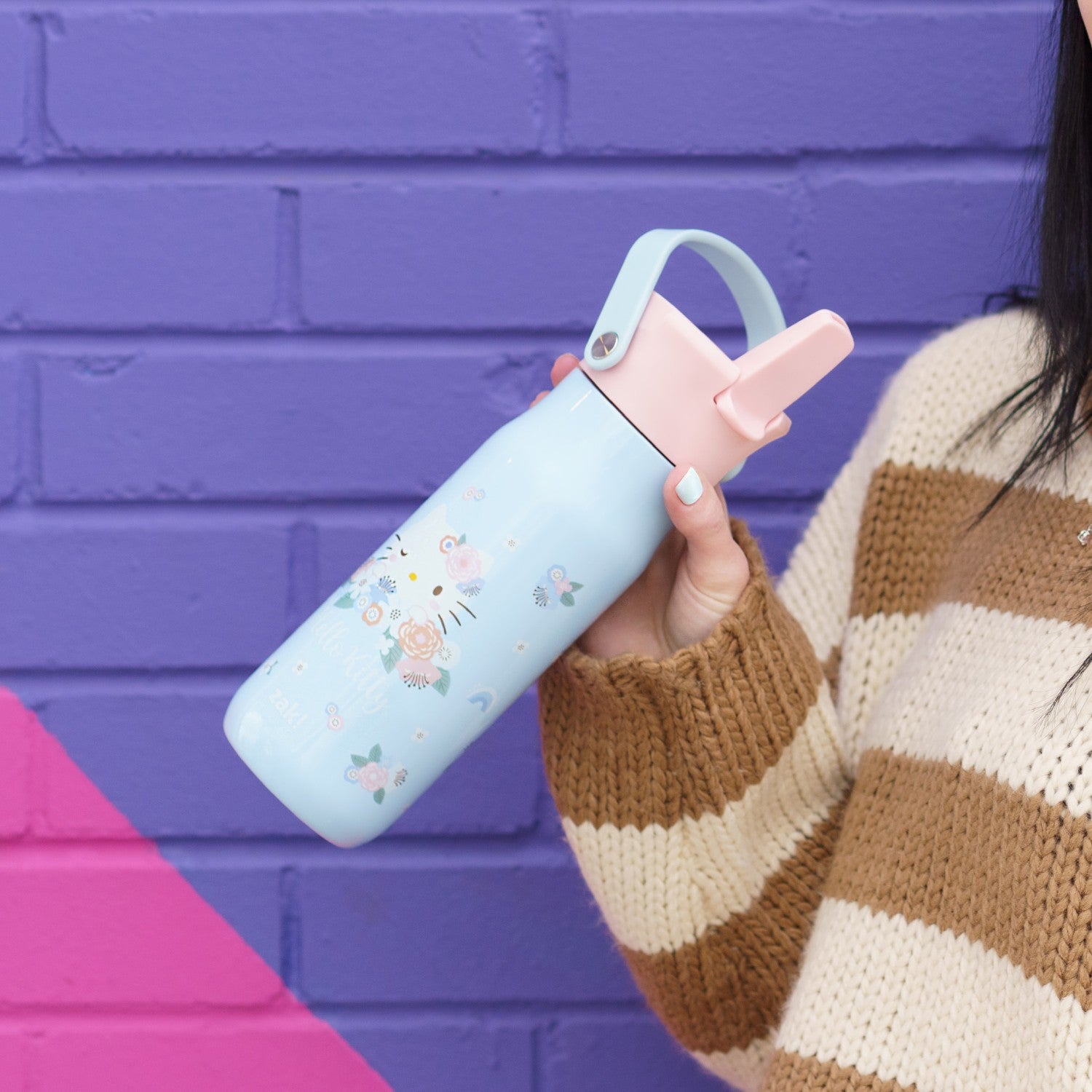 Person holding a light blue water bottle with a pink lid against a colorful wall.