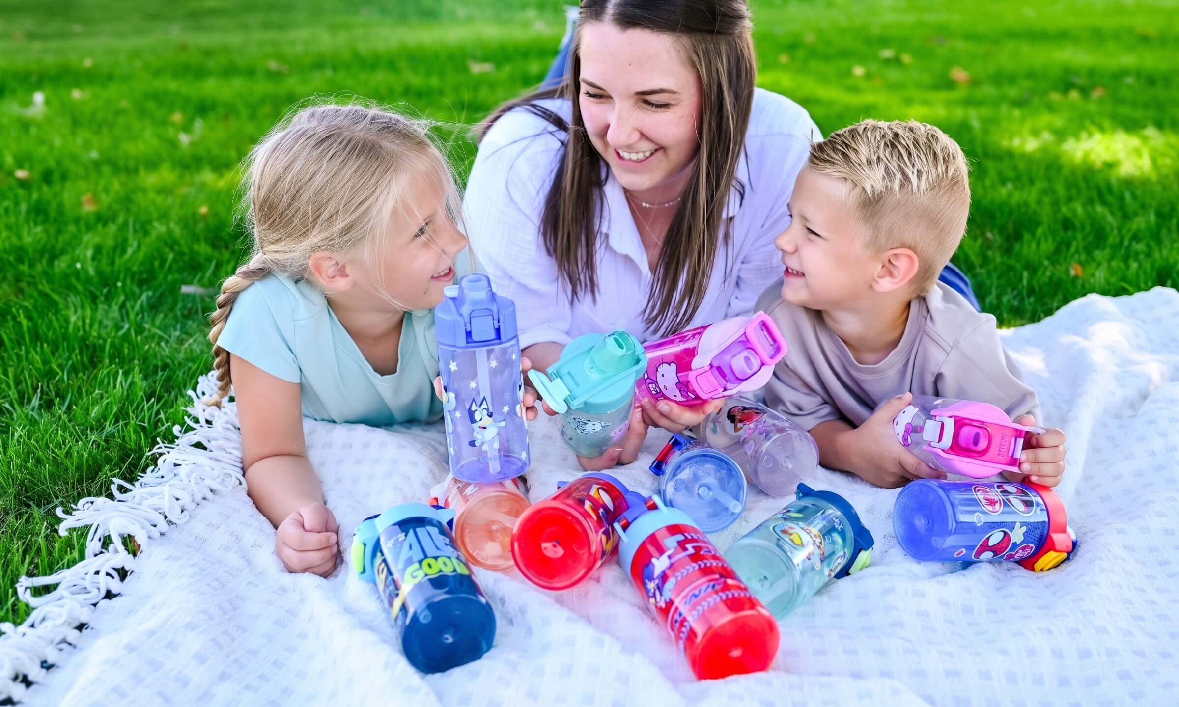 Mom and children happily sitting outside with colorful water bottles