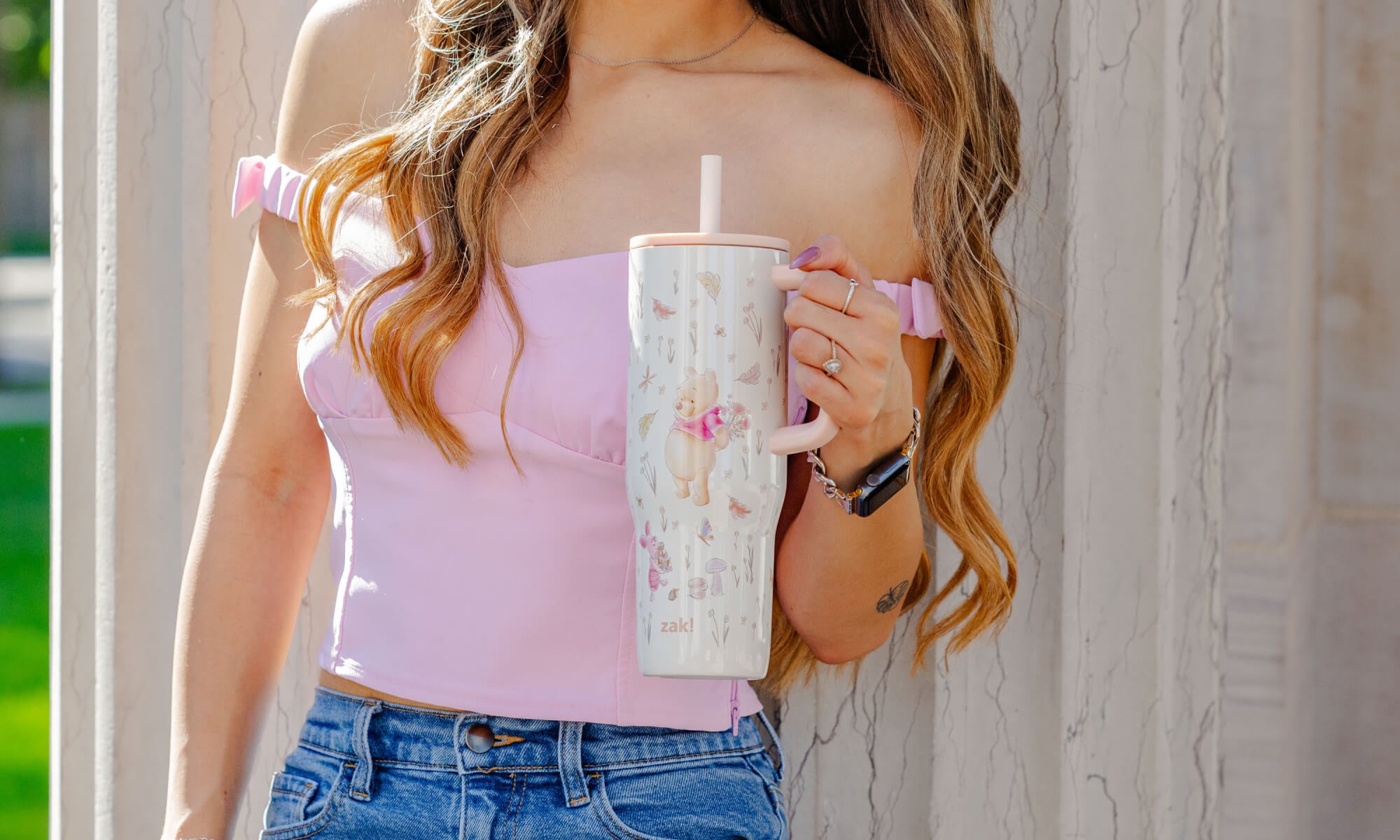 Person holding a Winnie the Pooh cup with a straw against a neutral background