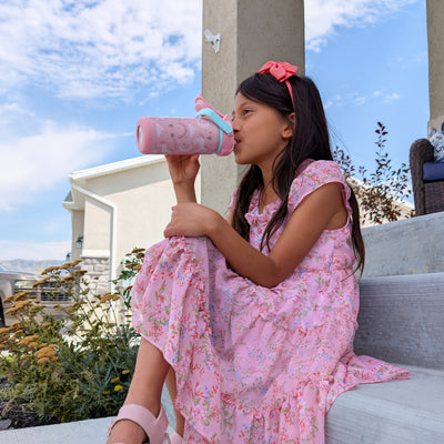 Girl sitting on step in pink dress sipping from pink zak water bottle