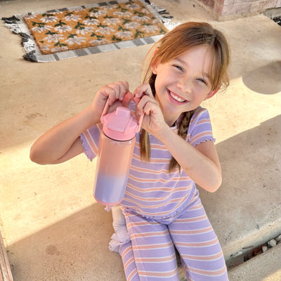 Girl holding pink and purple water bottle by the handle in natural light setting