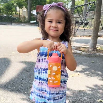 Girl outside holding a colorful orange and pink zak water bottle by the handle
