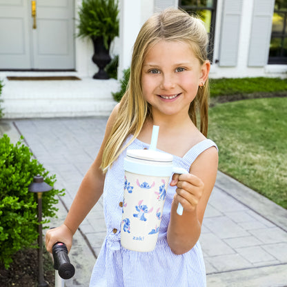 Young girl holding a zak tumbler with a straw, standing outside a house.