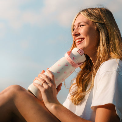 Girl holding white and pink water bottle outside on sunny day
