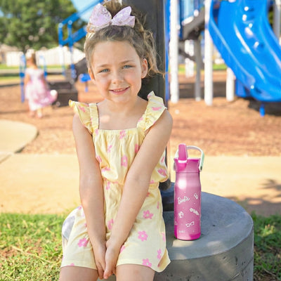 Girl at a park sitting next to Barbie water bottle with flip up spout