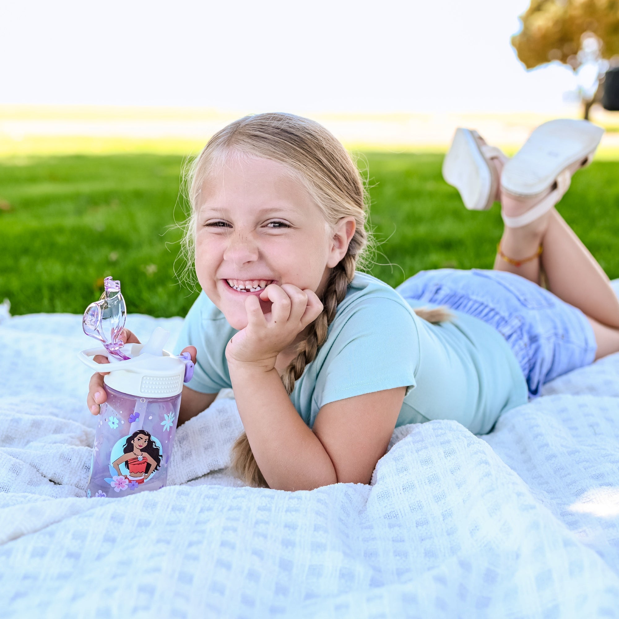 Girl sitting outside on white blanket holding a purple princess water bottle