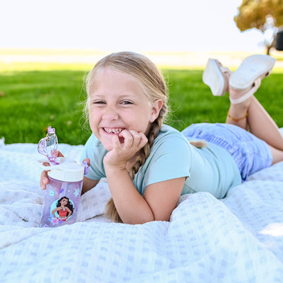Girl sitting outside on white blanket holding a purple princess water bottle