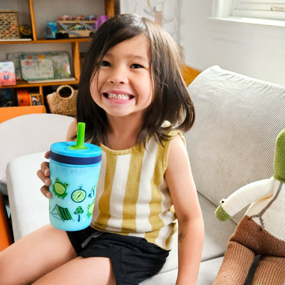 Child holding a blue zak! tumbler with green frog design on a couch