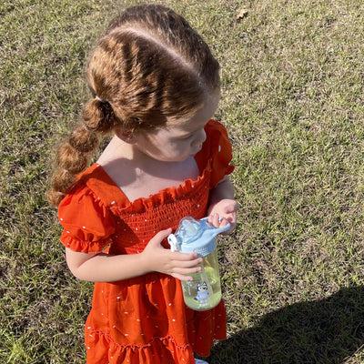 Girl in orange dress holding a green and blue kids water bottle