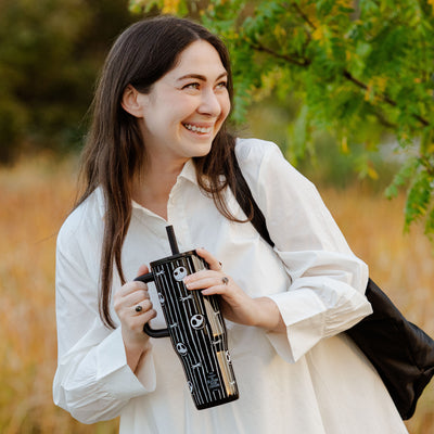 Woman in white top carrying zak! black and white travel tumbler